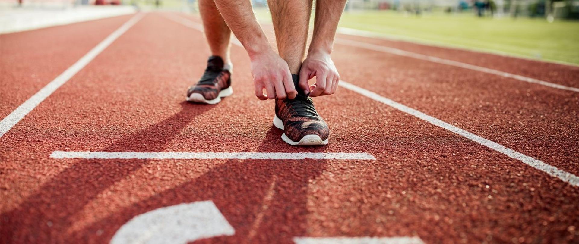 Sportowiec na bieżni, sprawdzający wiązanie obuwia, przed startem. Widok na ręce i buty.