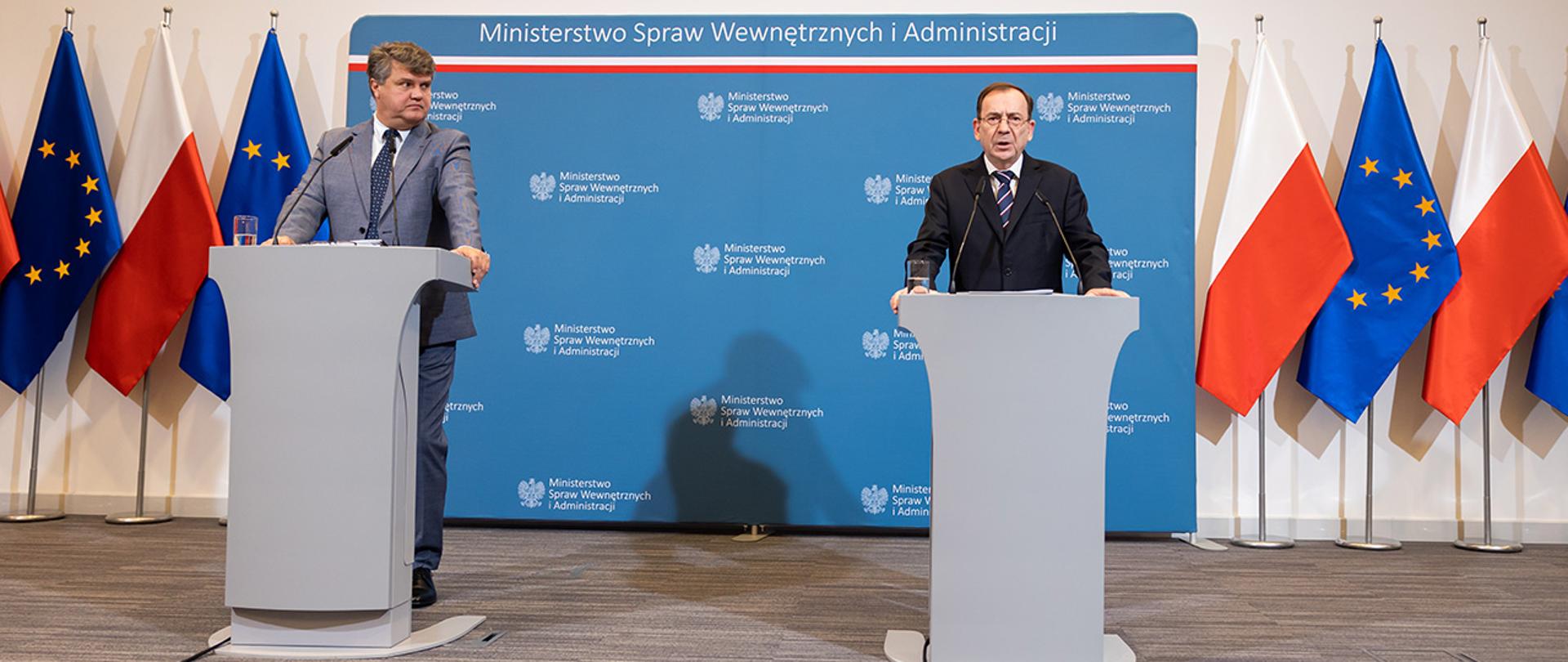 Na zdjęciu widać ministra Mariusza Kamińskiego i wiceministra Macieja Wąsika stojących za mównicami w trakcie konferencji prasowej.